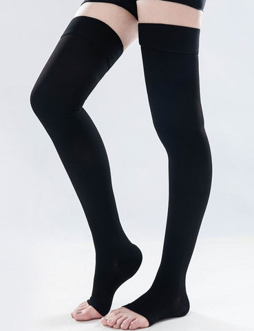 The image shows a legs of a woman standing with the right leg slightly bent forward and wearing black color open toe compression socks.