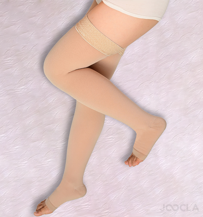 Woman's leg lying on the bed wearing beige color Thigh High Open-Toe Compression Socks.
