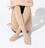 Woman in sitting position in cross legs wearing beige color thigh-high closed-toe compression socks.